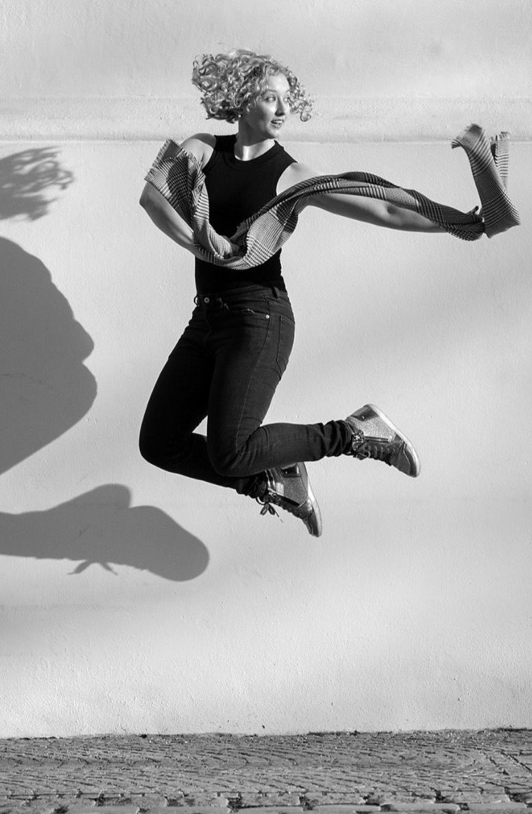 A black and white photo of Louisa Poletti jumping while holding a scarf