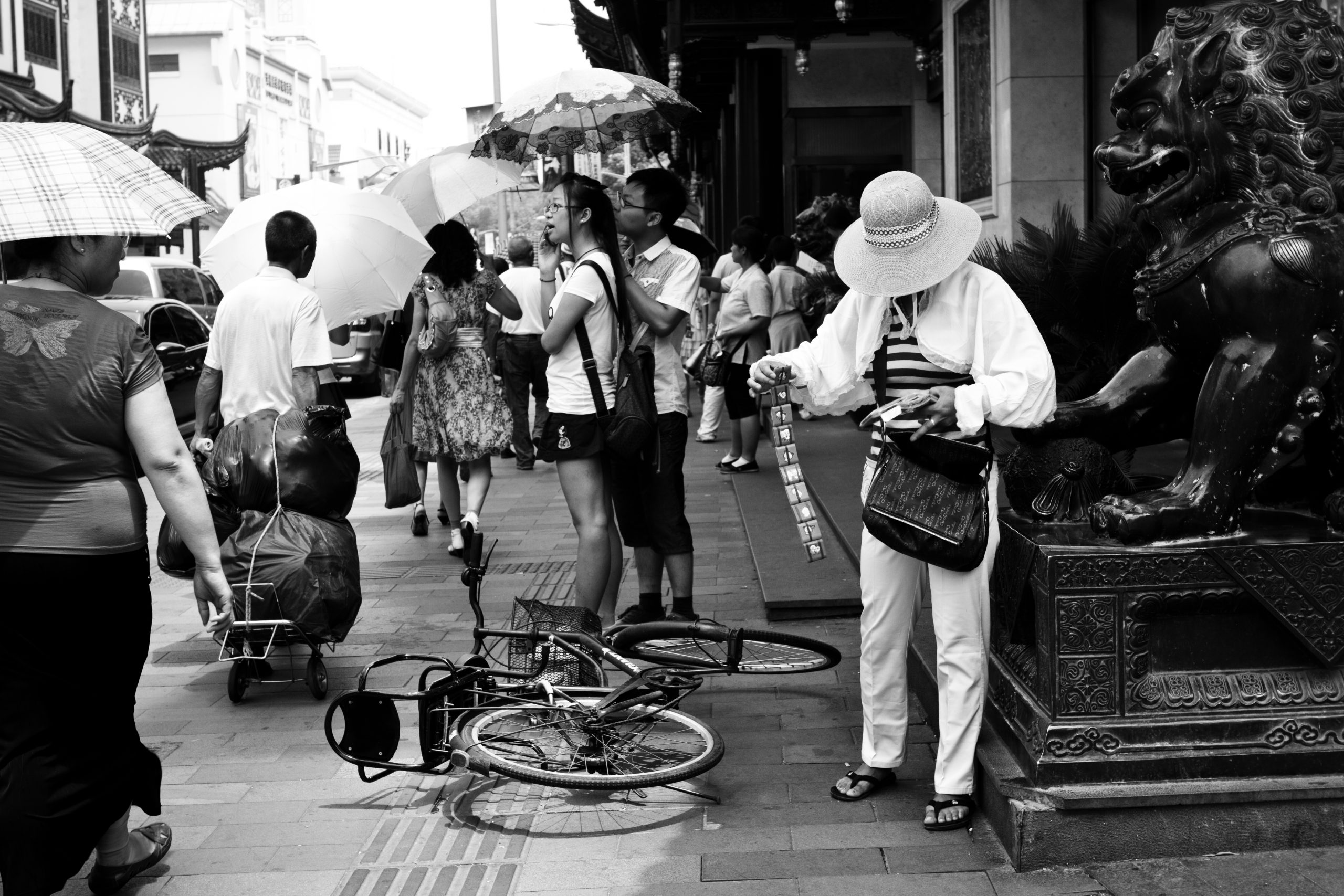 A lady selling unfolding trinkets on a busy street next to a collapsed bicycle